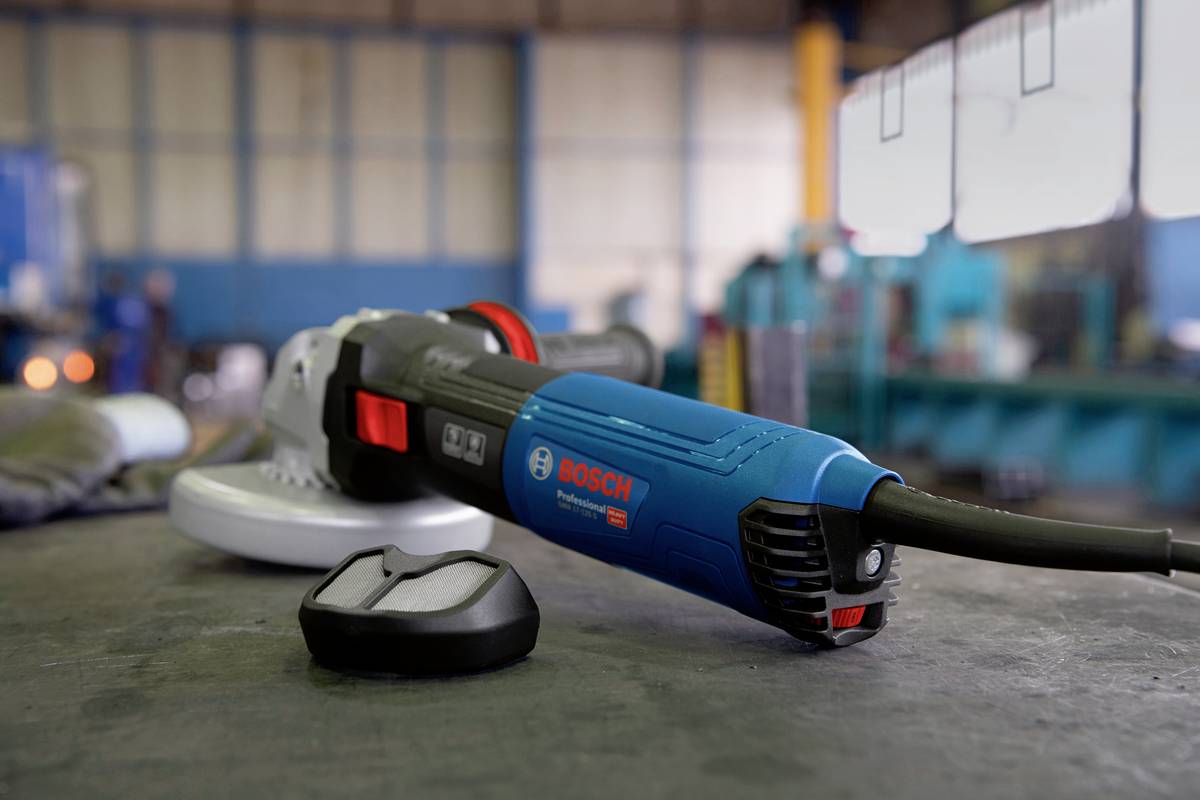 Ein blauer Winkelschleifer liegt auf einem Tisch in einer Werkstatt. Links daneben liegt ein Metallstück. Im Hintergrund unscharfe Maschinen.