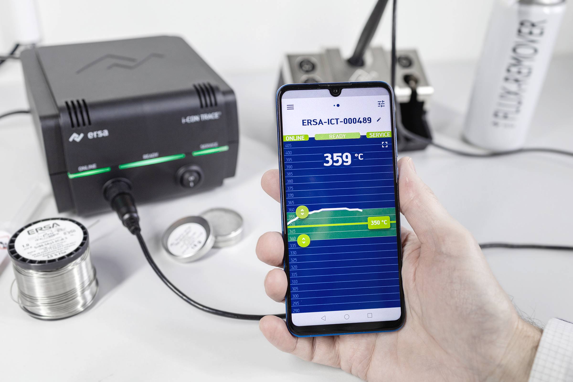 Hand hält ein Smartphone mit Temperaturanzeige von 359 °C. Im Hintergrund eine Lötstation mit Lötzinnrollen und Markenname sichtbar.