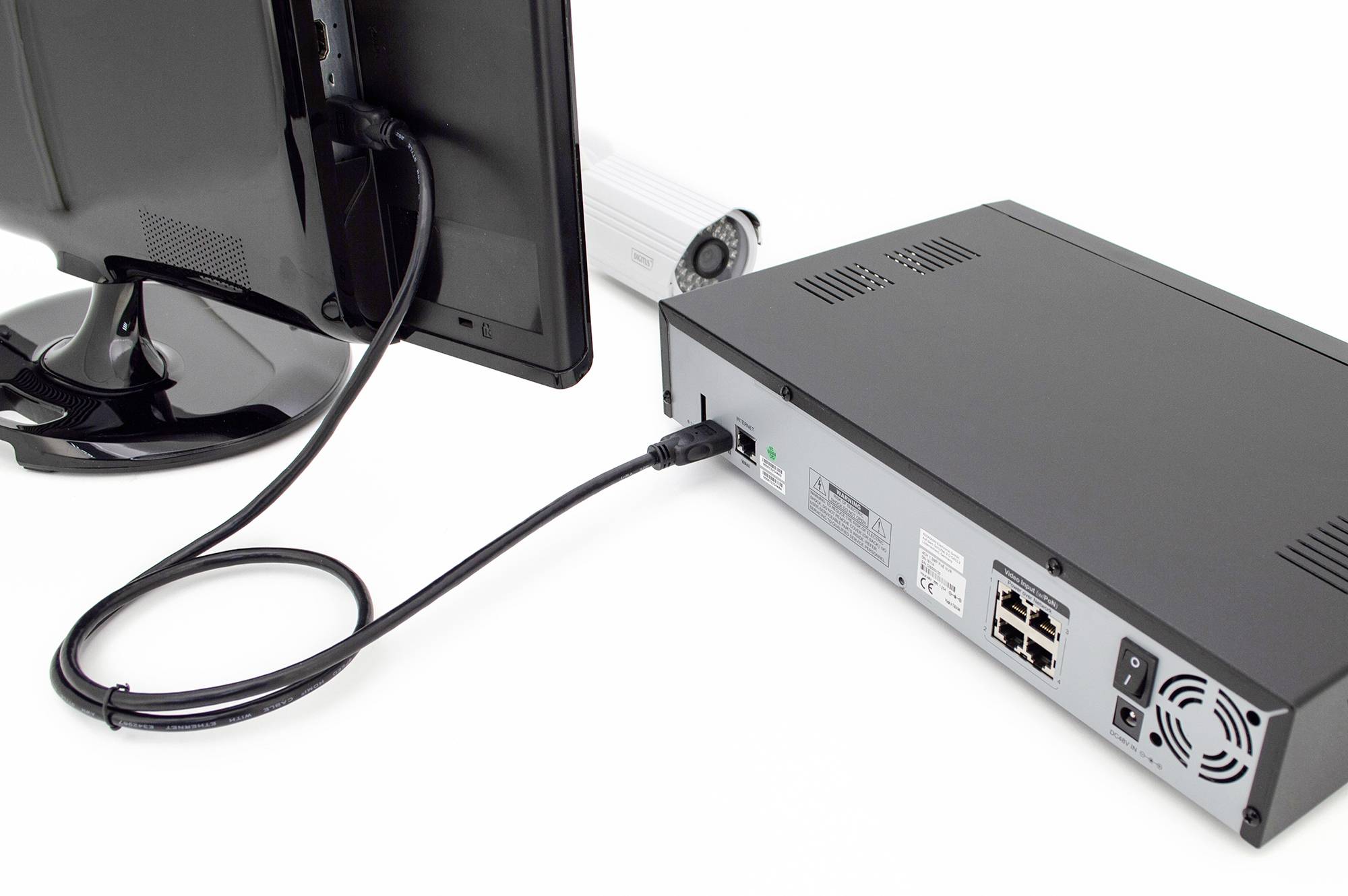 Ein Monitor ist mit einem schwarzen Kasten verbunden, der Netzwerkkabel und Anschlüsse zeigt. Eine Kamera liegt im Hintergrund.