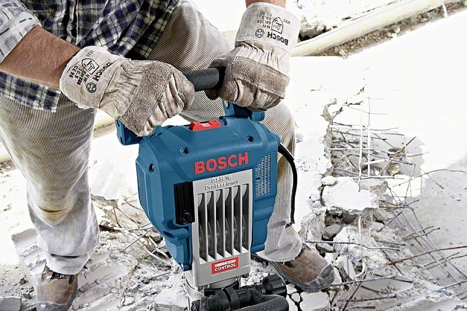 Eine Person bedient einen Bosch-Abbruchhammer, um Beton zu durchbrechen. Der Boden ist teilweise aufgerissen, Bewehrung ist sichtbar.