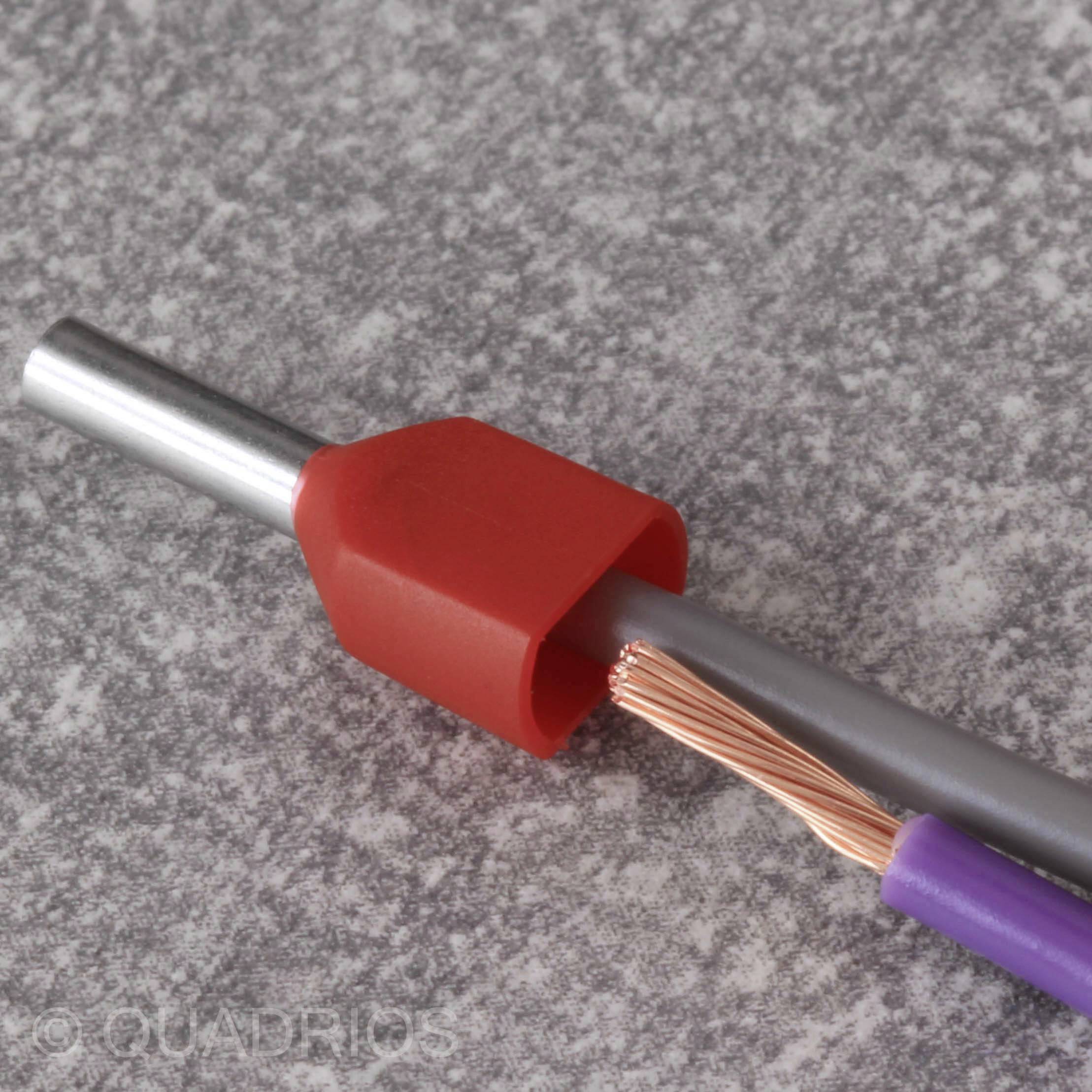 Ein graues Kabel mit roten Isolierhülsen und freigelegtem Kupferdraht liegt auf einer grauen Oberfläche.