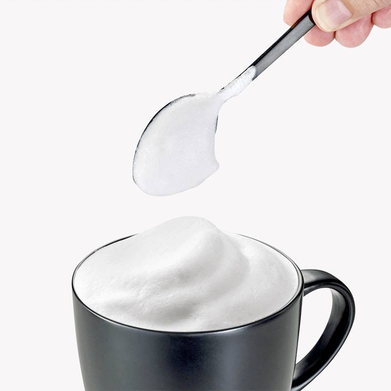 Ein Löffel mit Milchschaum wird über eine Tasse mit aufgeschäumter Milch gehalten.