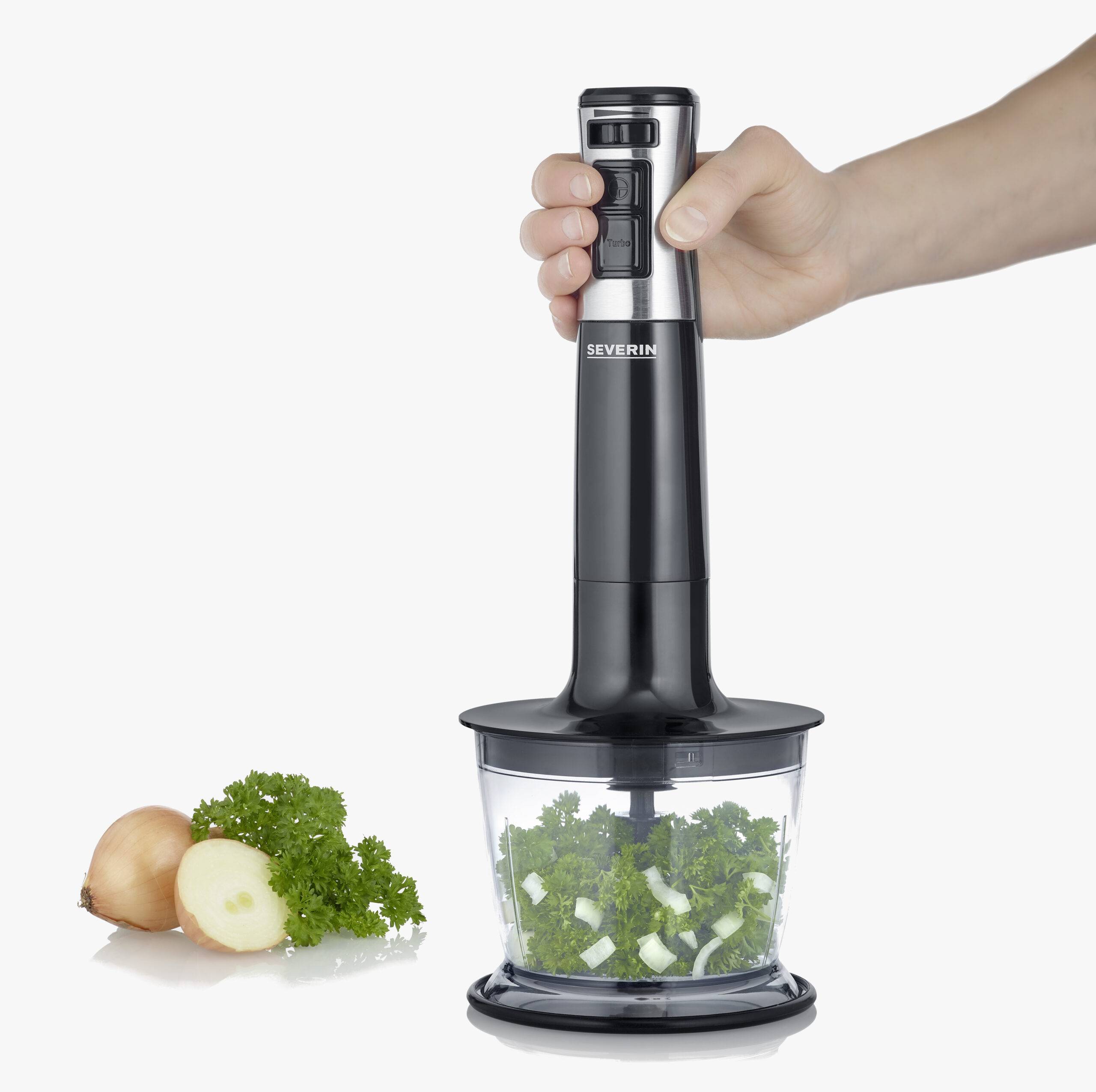 Handmixer zerkleinert frische Kräuter und Zwiebeln in einem transparenten Behälter