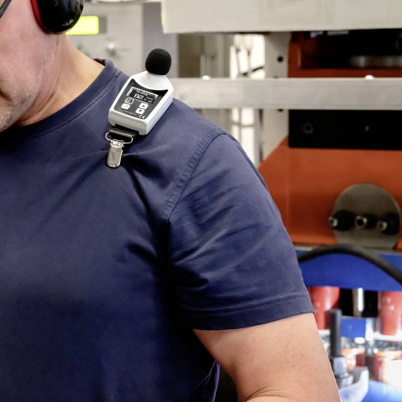 Ein Mann trägt ein Mikrofon und ein tragbares Gerät, möglicherweise für Kommunikation oder Audioaufzeichnung, in einer industriellen Umgebung.