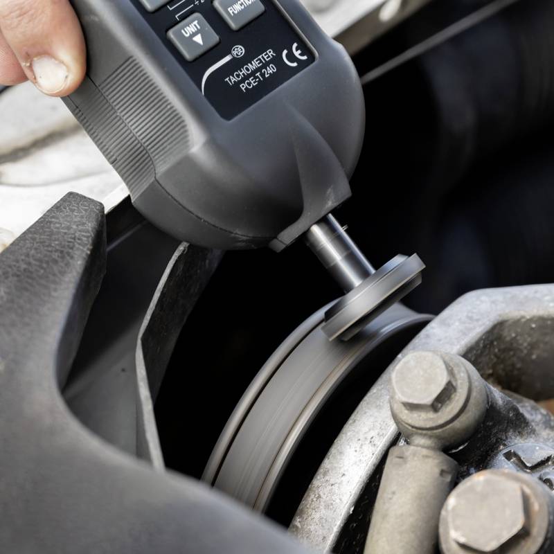 Eine Person misst mit einem Tachometer die Drehzahl eines rotierenden Objekts, vermutlich eines Maschinenteils.