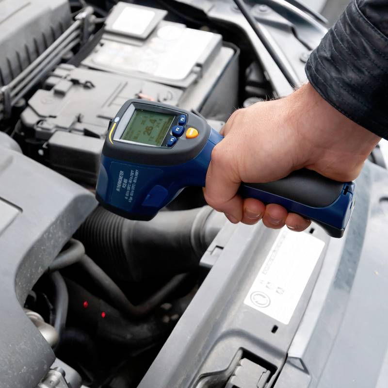 Eine Person überprüft den Motor eines Autos mit einem digitalen Thermometer, um die Temperatur zu messen.