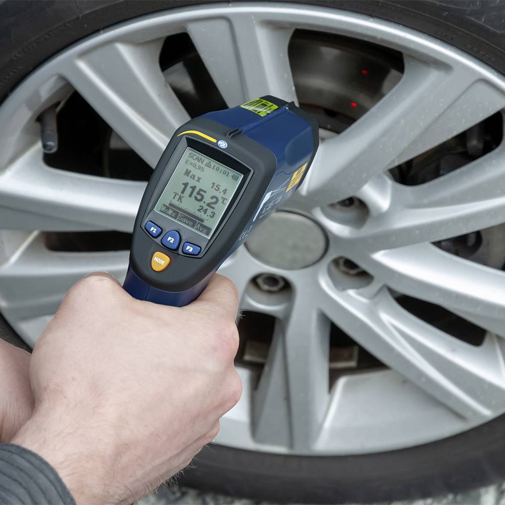 Eine Person misst die Temperatur eines Autoreifens mit einem Infrarot-Thermometer. Das Display zeigt 115,2 Grad Fahrenheit an.
