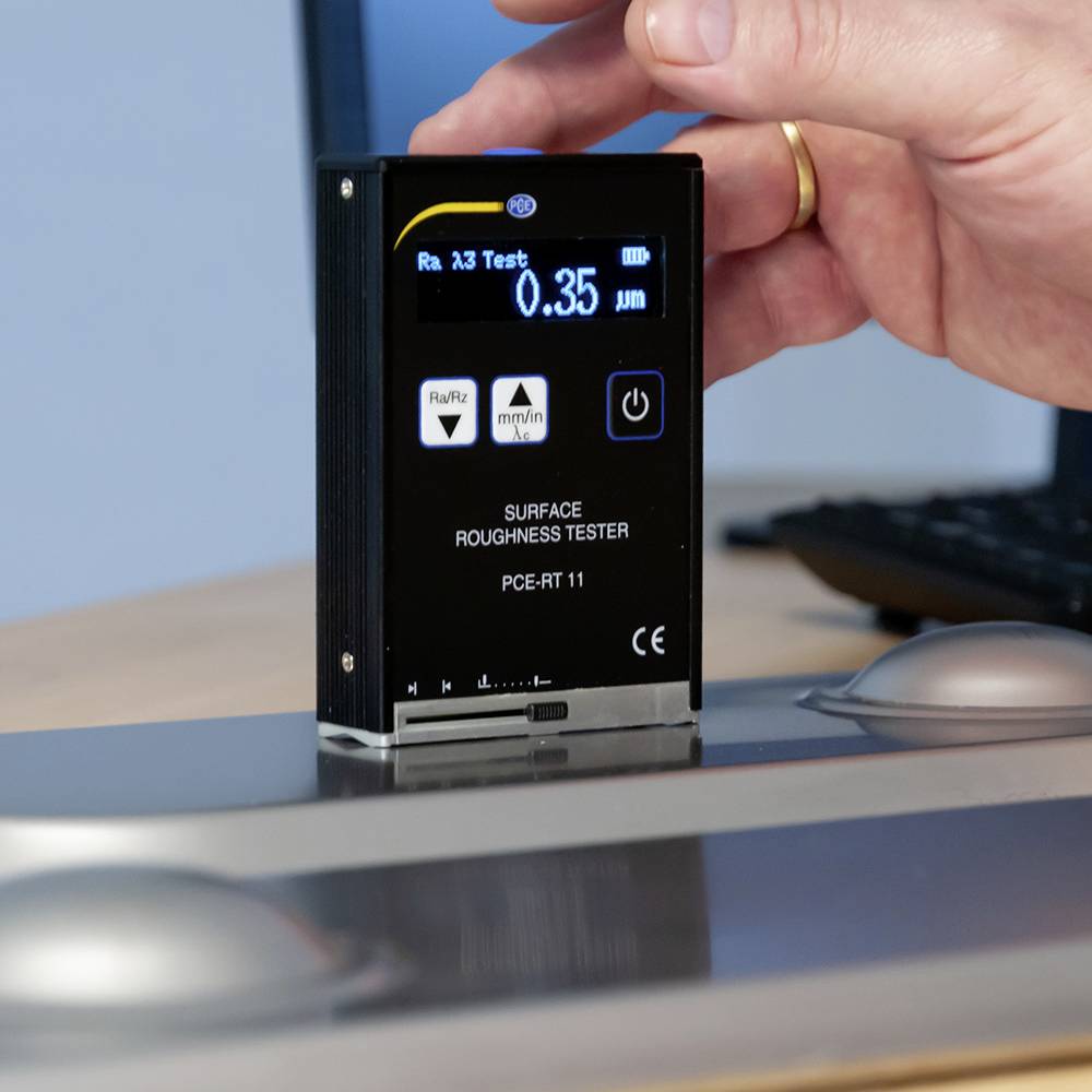 Ein Hand hält ein Rauheitsmessgerät, das auf einem Metallobjekt ruht. Das Display zeigt 'Ra', '0,35 µm' und andere Messparameter.