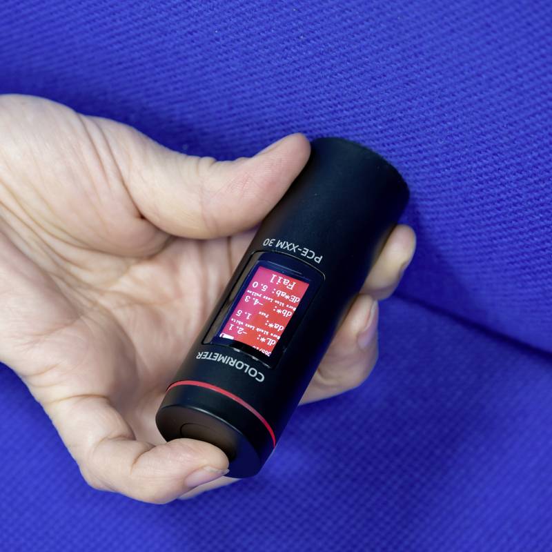 Hand hält ein schwarzes, zylinderförmiges Gerät mit digitalem Display und rotem Hintergrund, das Temperaturwerte anzeigt. Hintergrund blau.