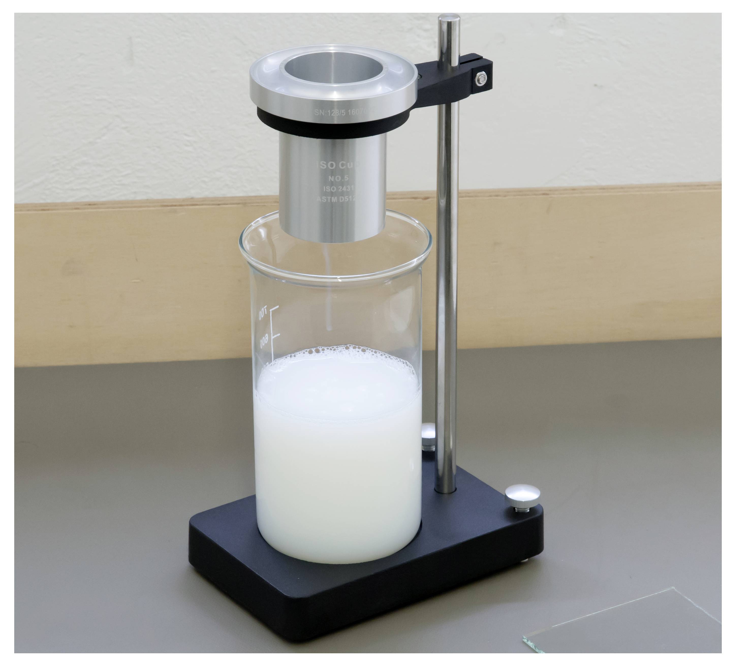 Laborgerät mit einem an einem Ständer aufgehängten zylindrischen Metallmischer über einem Becher mit schäumiger weißer Flüssigkeit.