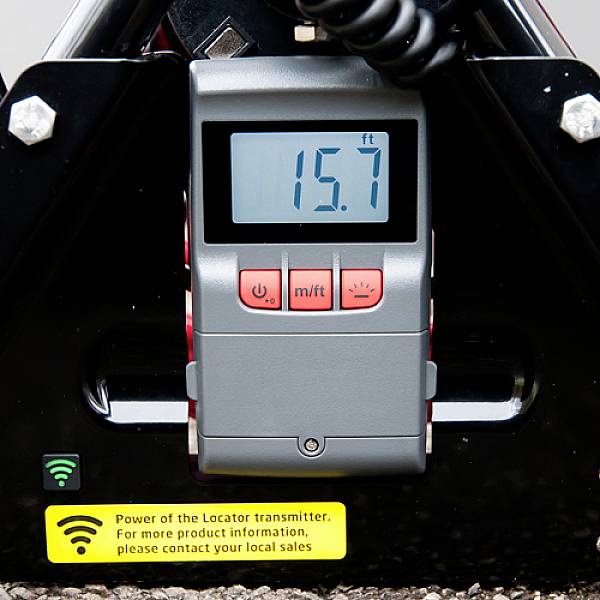 Ein digitales Messgerät zeigt '15.7 ft' auf einem Display. Dazu ein Symbol, das auf die Stromversorgung des Senders hinweist.