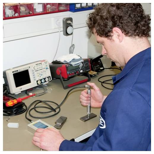 Techniker testet ein elektronisches Gerät auf einer Werkbank und hält ein sondenartiges Werkzeug neben Laborgeräte und Kabel.