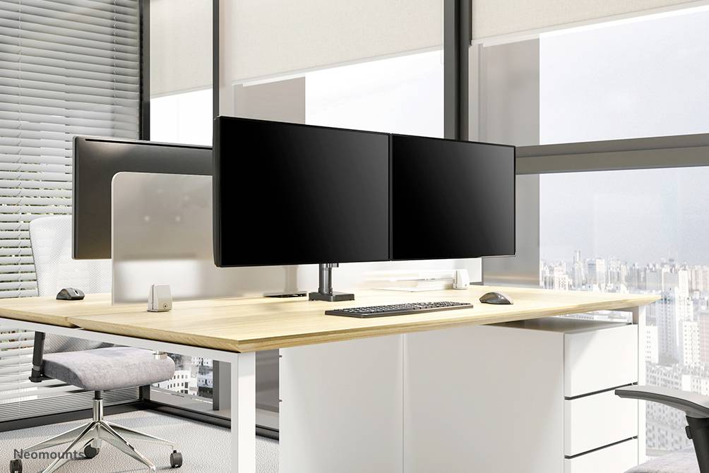 Ein modernes Büro mit einem großen Schreibtisch, zwei Monitoren, Tastatur, Maus und einem Bürostuhl. Große Fenster bieten eine Stadtansicht.