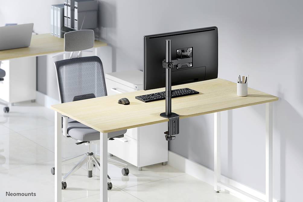 Ein moderner Schreibtisch mit Monitor, Tastatur und Maus, ergonomisch eingerichtet. Hintergrund zeigt weiteres Büro mit Schreibtisch.