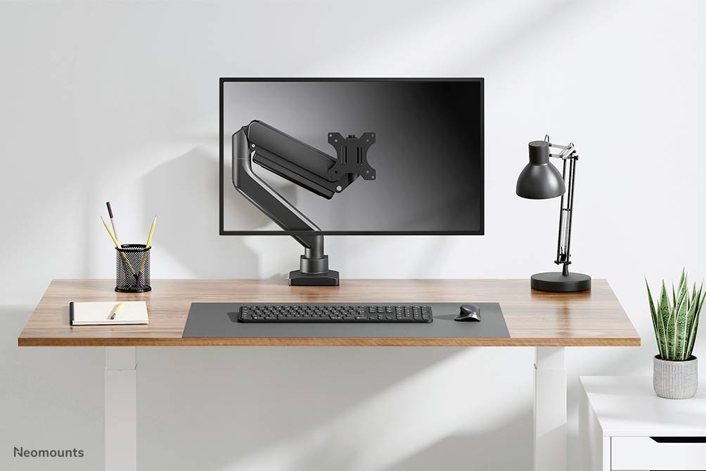 Höhenverstellbarer Schreibtisch mit Monitorhalterung, Monitor, Tastatur, Lampe und Stifthalter; minimalistisches Arbeitszimmer.