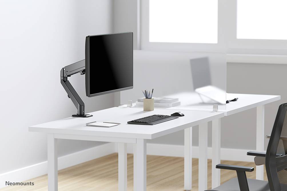 Ein moderner, weißer Schreibtisch mit einem Monitor an einem beweglichen Arm, einer Tastatur und Büroartikeln. Heller Raum mit großen Fenstern.
