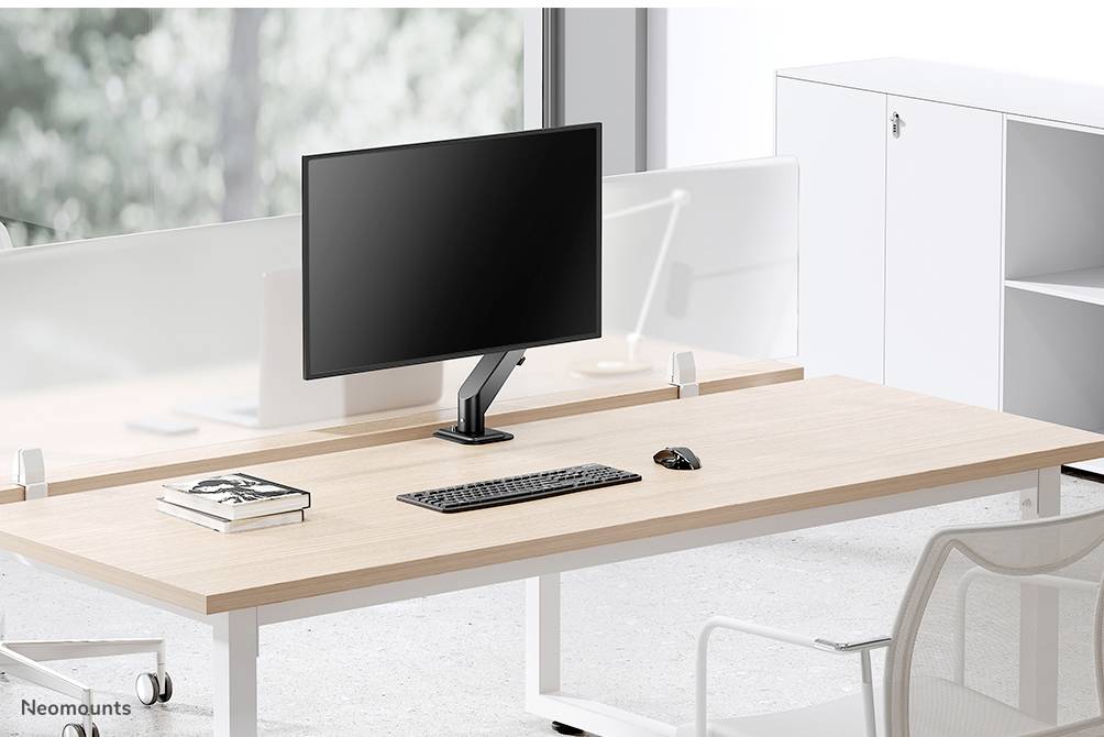 Ein moderner Schreibtisch mit Holzplatte, darauf stehen ein Computerbildschirm, Tastatur und Maus; Bürostuhl und Regal im Hintergrund.