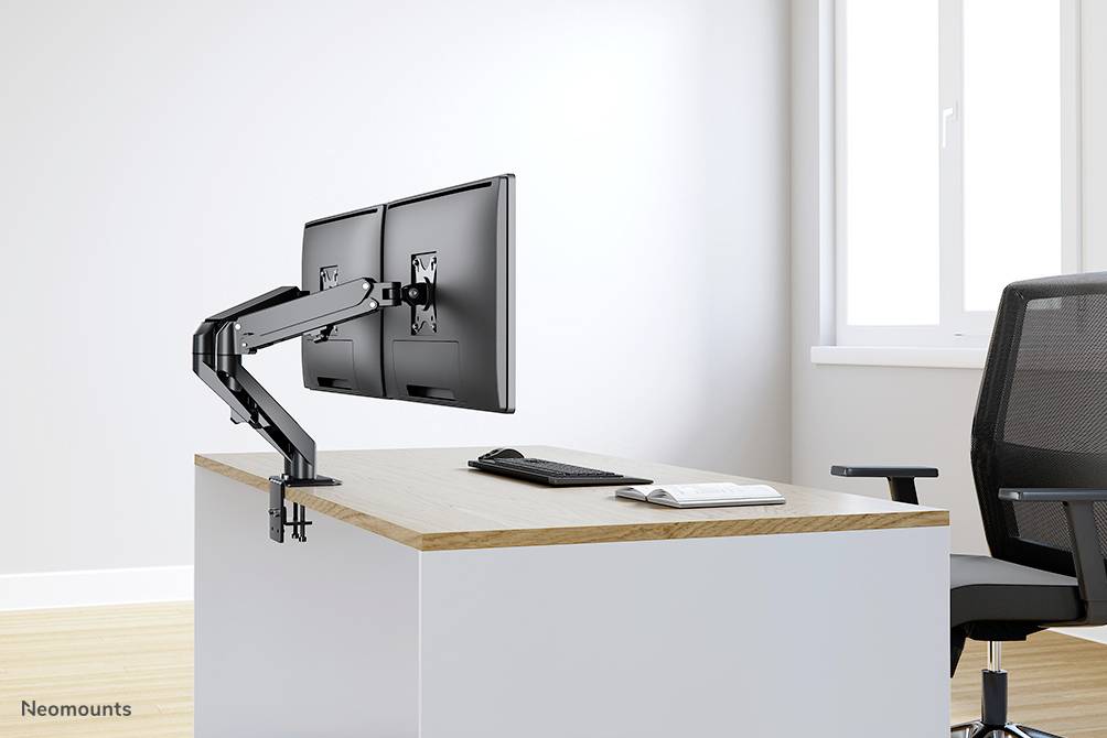 Zwei Monitore an einem flexiblen Armhalter auf einem Schreibtisch mit Tastatur und Maus. Ein leerer Stuhl steht daneben.
