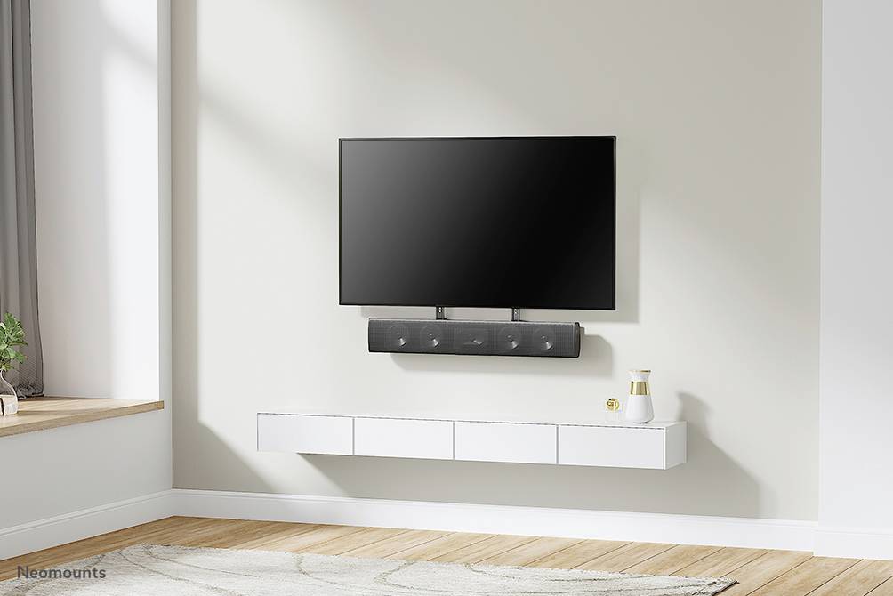 Ein Flachbildfernseher und eine Soundbar sind an einer hellen Wand montiert. Darunter ein schwebendes Sideboard mit Dekoration.