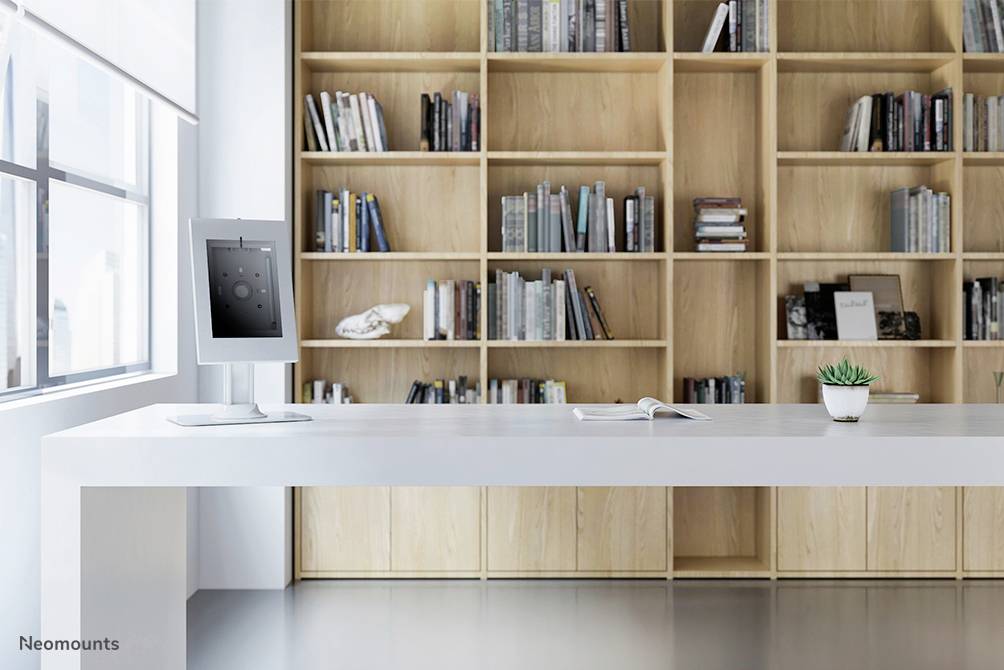 Ein moderner, minimalistisch eingerichteter Raum mit einem weißen Tisch, auf dem ein Monitor und ein Buch stehen, vor einem Holzregal voller Bücher.