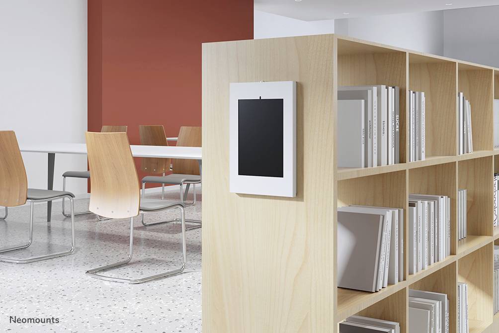 Moderner Bibliotheksraum mit Bücherregal, hölzernen Stühlen und einem roten Akzent an der Wand. Ein Tablet ist an einem Regal befestigt.