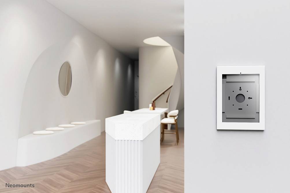 Moderner, minimalistischer Innenraum mit weißen Wänden und einem kleinen Empfangstresen. An der Wand hängt ein rechteckiger, grauer Rahmen.