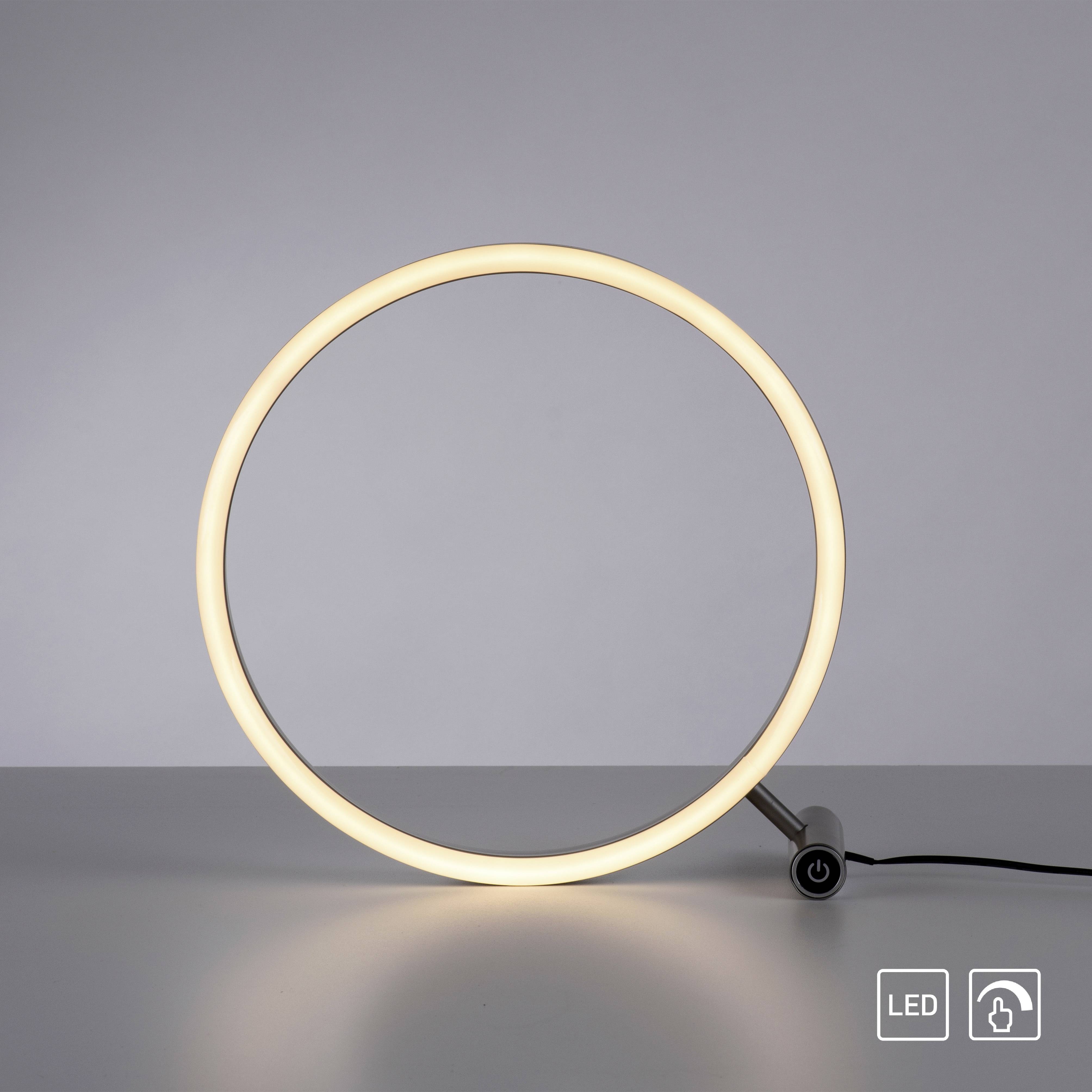 Eine LED-Tischlampe in Form eines leuchtenden Rings steht auf einem Tisch. Unten rechts sind Tasten für LED und Power-Symbol sichtbar.