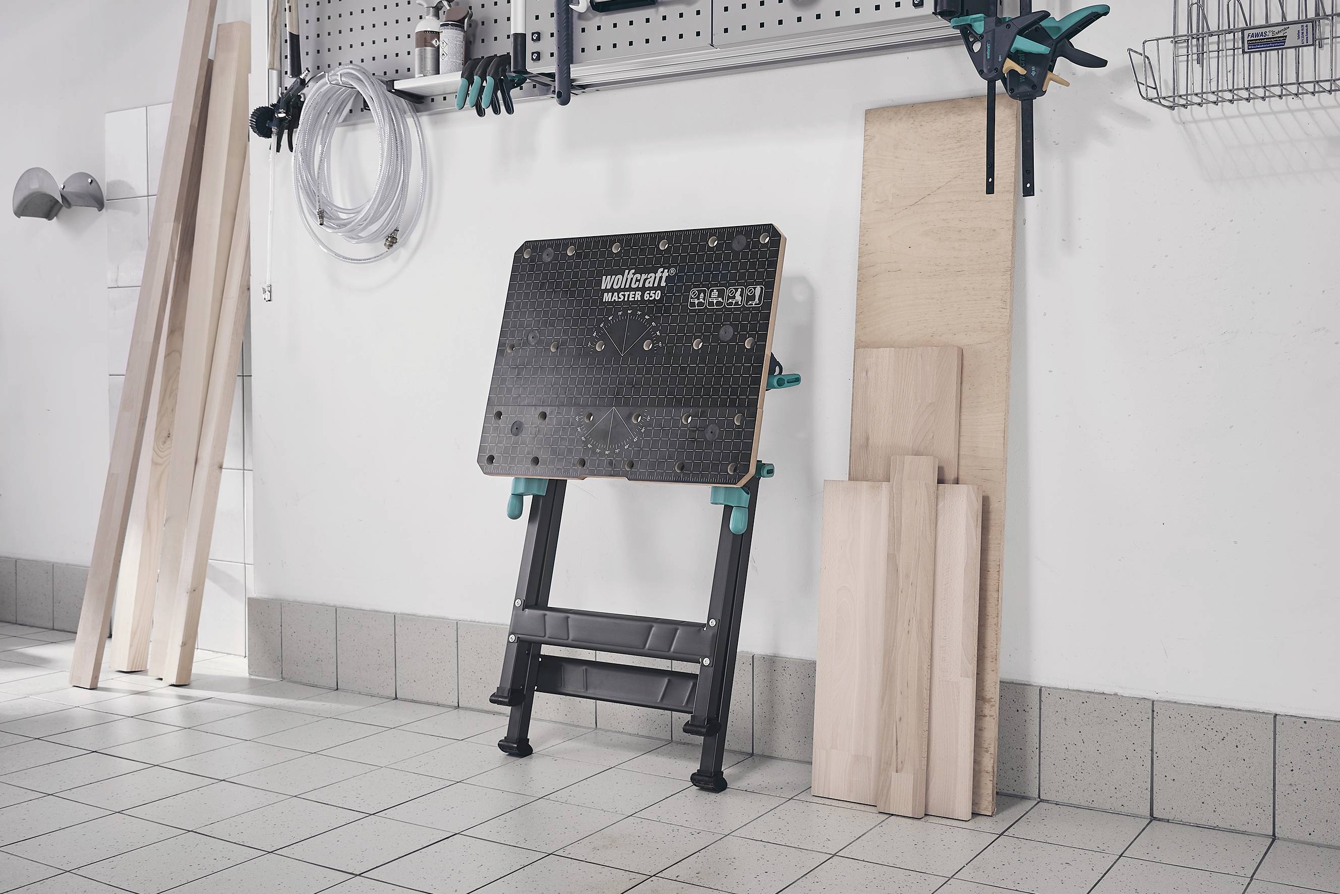 Arbeitsplatz in einer Werkstatt mit Werkbank und Holzmaterialien an der Wand.