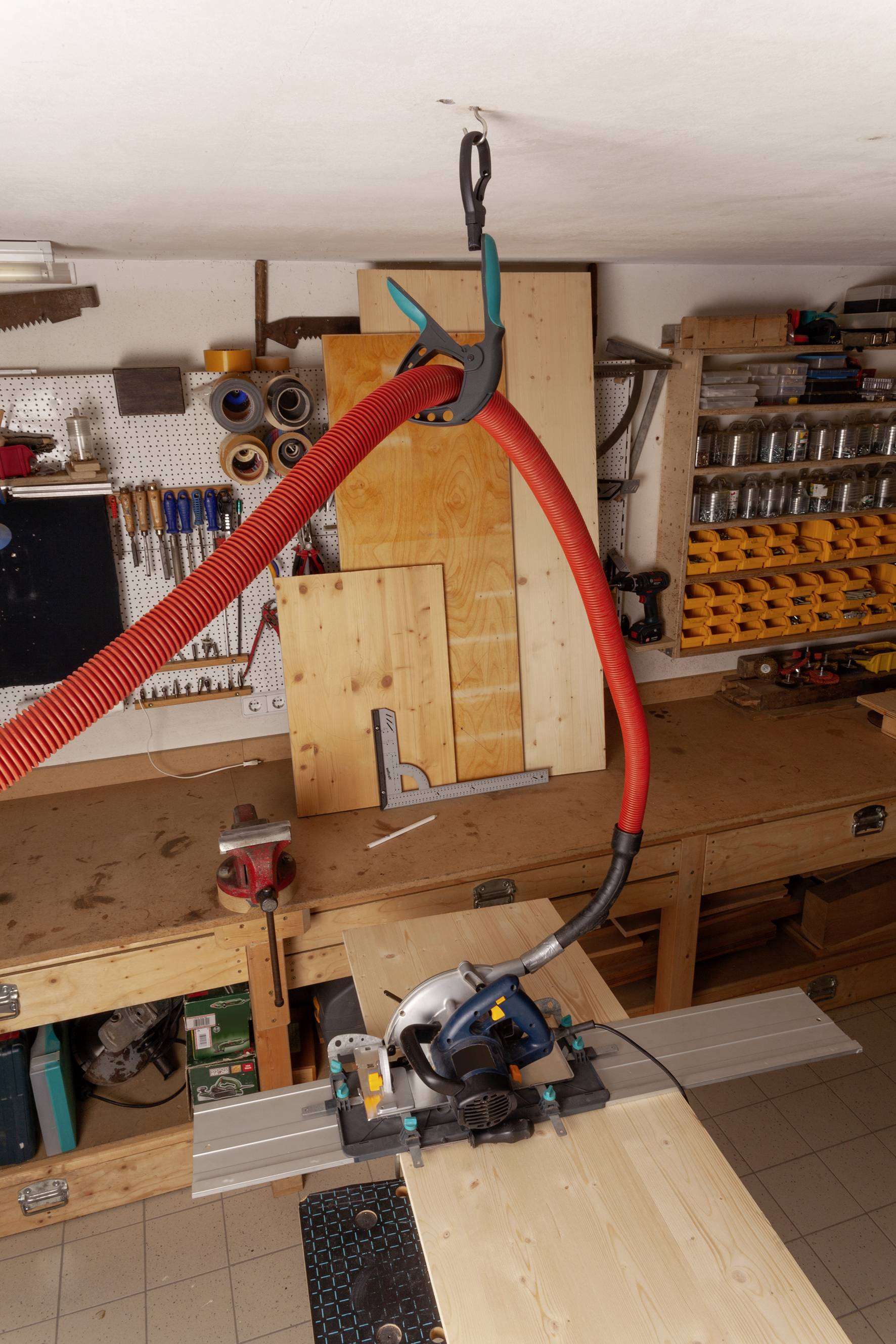 Werkstatt mit Holzbearbeitung: Eine Kreissäge schneidet ein Holzbrett auf einem Tisch. Werkzeuge und Materialien sind im Hintergrund organisiert.