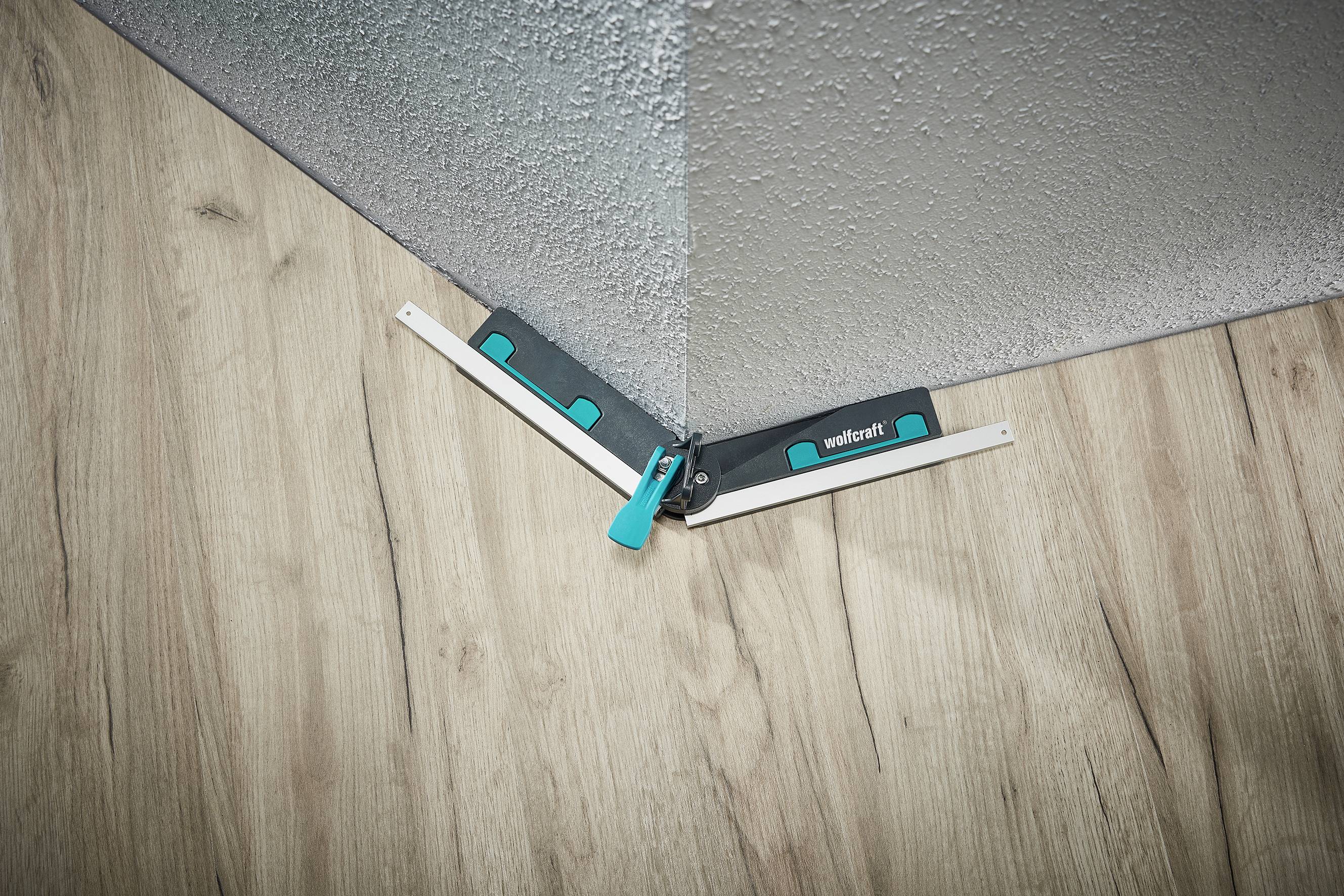 Ein Winkelmesswerkzeug in einer Zimmerecke auf Holzfußboden und an einer grauen Wand, zeigt präzise den Winkel der Ecke.