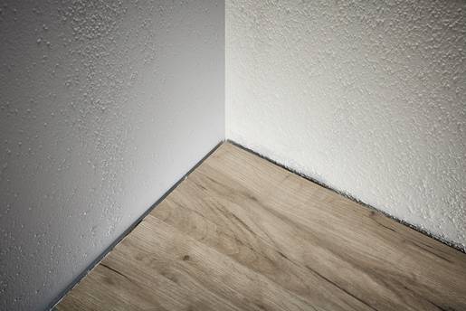 Ecke eines Raumes mit Holzboden und weiß verputzten Wänden.