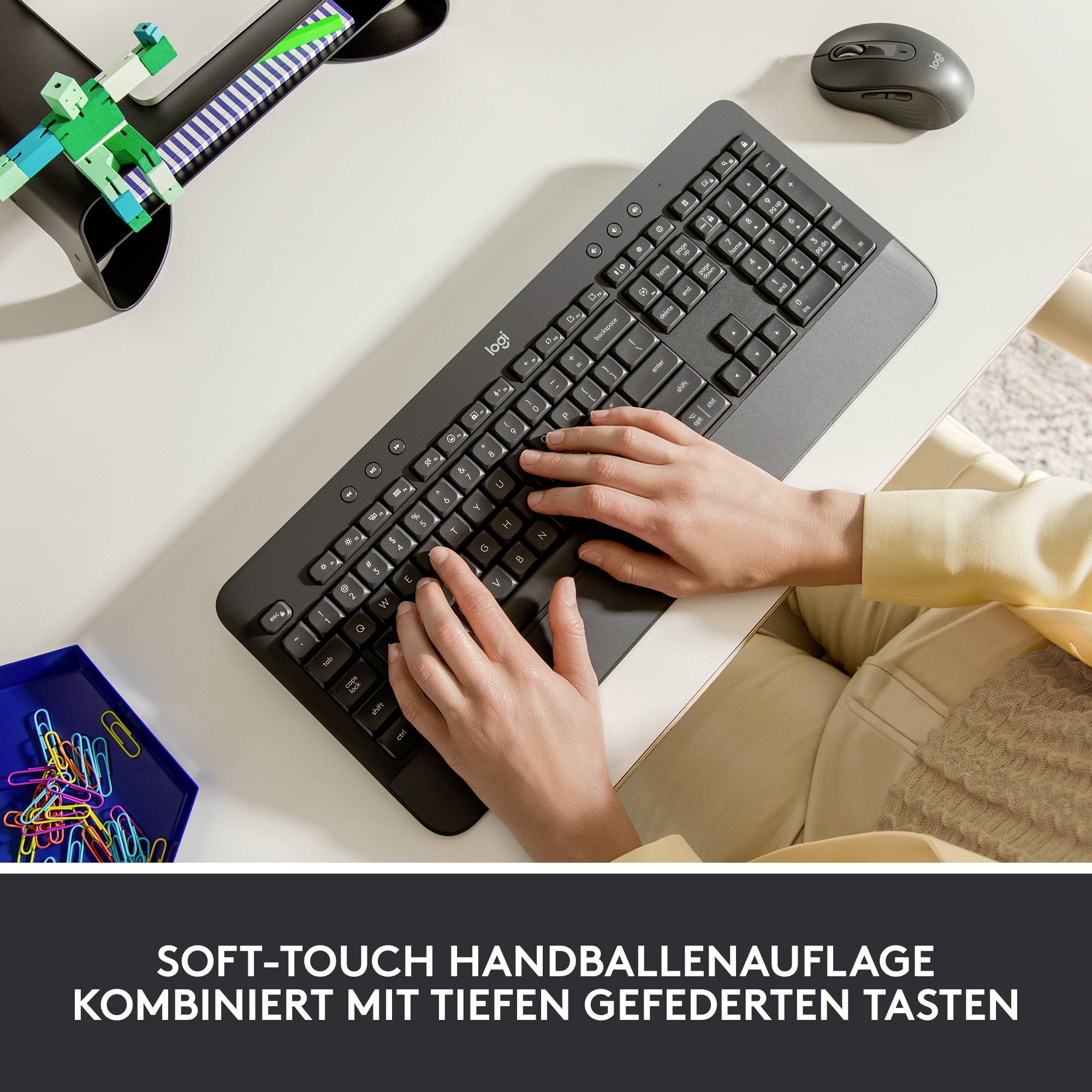 Eine Person tippt auf einer schwarzen Tastatur mit einer Soft-Touch-Handballenauflage. Text im Bild: 'Soft-Touch Handballenauflage kombiniert mit tiefen gefederten Tasten'.