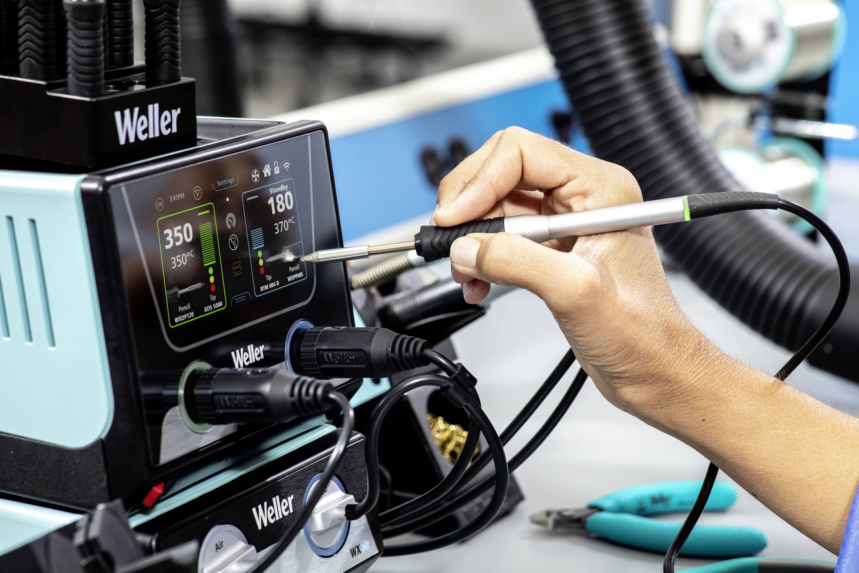 Eine Person hält einen Lötkolben, der mit einer Steuerungsstation von Weller verbunden ist, auf einem Arbeitstisch.