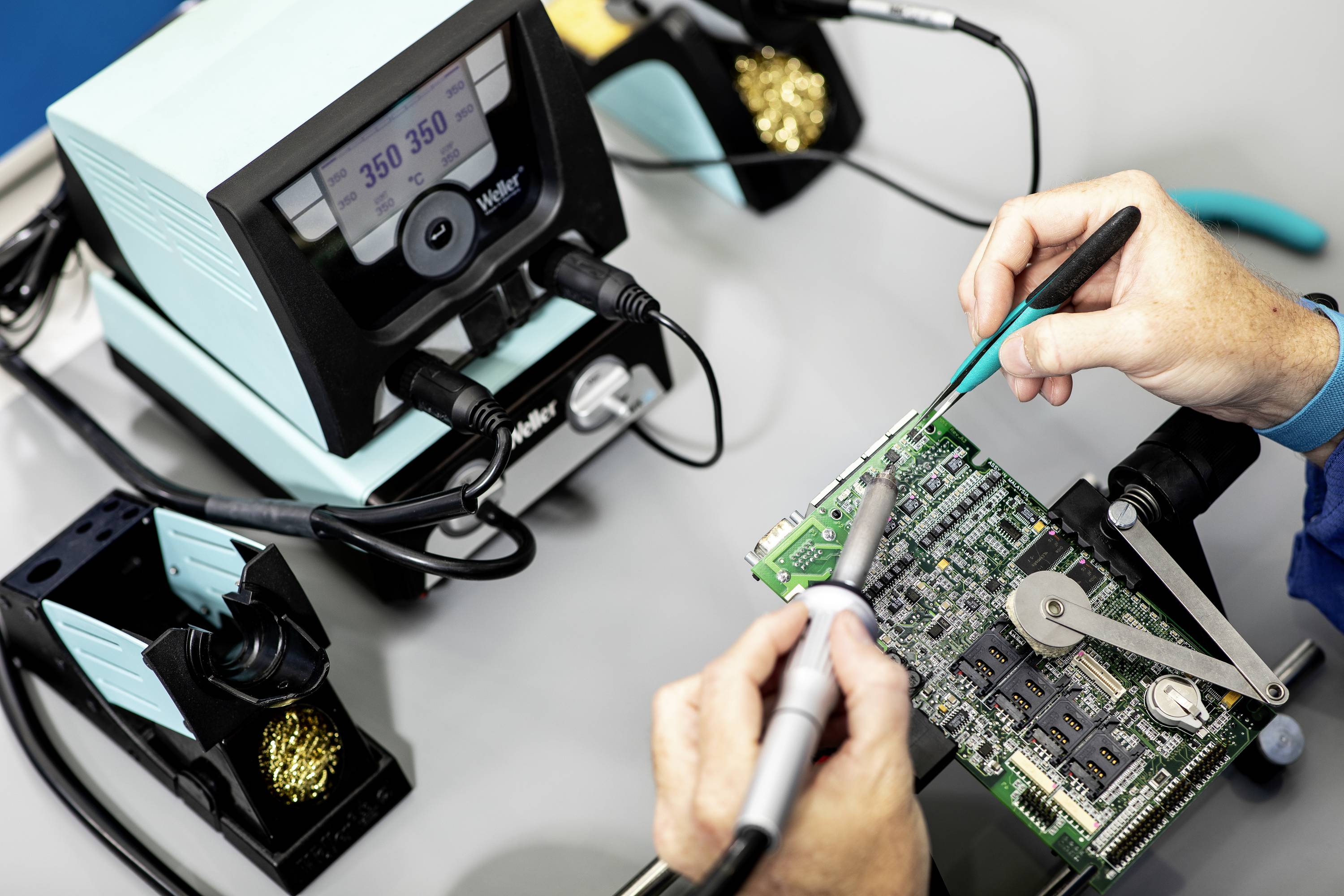 Eine Person repariert eine Leiterplatte mit einem Lötkolben, Pinzette und digitalem Lötkolben. Nahaufnahme des technischen Prozesses.