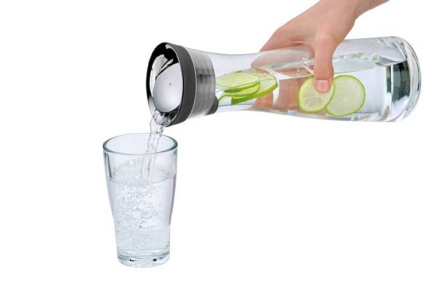 Eine Hand gießt Wasser mit Limettenscheiben aus einer Karaffe in ein Glas.
