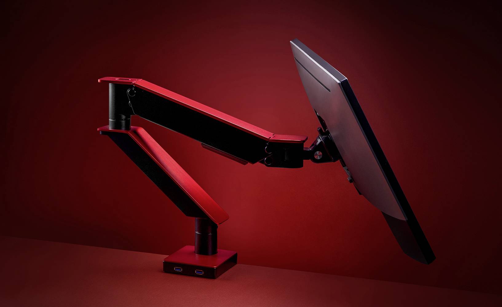 Ein ergonomischer Monitorarm in Rot, hält einen Bildschirm in einer schwebenden Position vor einem roten Hintergrund.