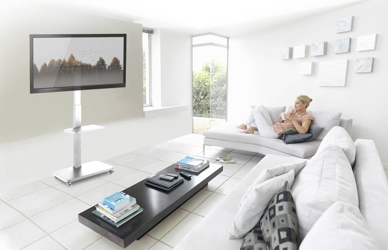 Eine Frau sitzt entspannt auf einem Sofa und trinkt Kaffee, während sie einen großen Flachbildfernseher in einem hellen Wohnzimmer betrachtet.