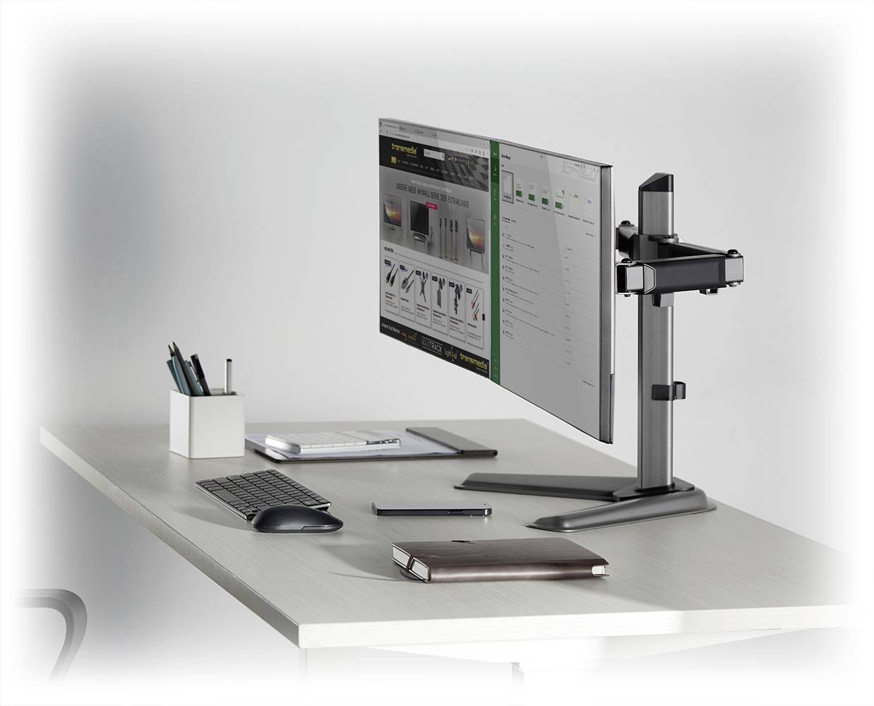 Ein stilvoll eingerichteter Schreibtisch mit Computerbildschirm, Tastatur, Notizbuch und Stiftehalter auf einem modernen weißen Tisch.