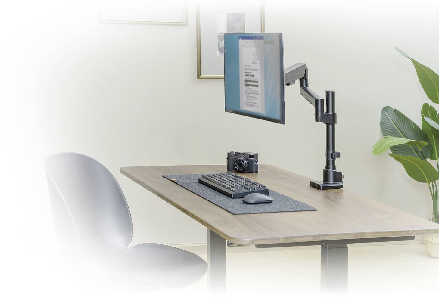 Ein Schreibtisch mit einem montierten Bildschirmarm, Tastatur, Mauspad und Kamera ist abgebildet, daneben steht ein Stuhl.