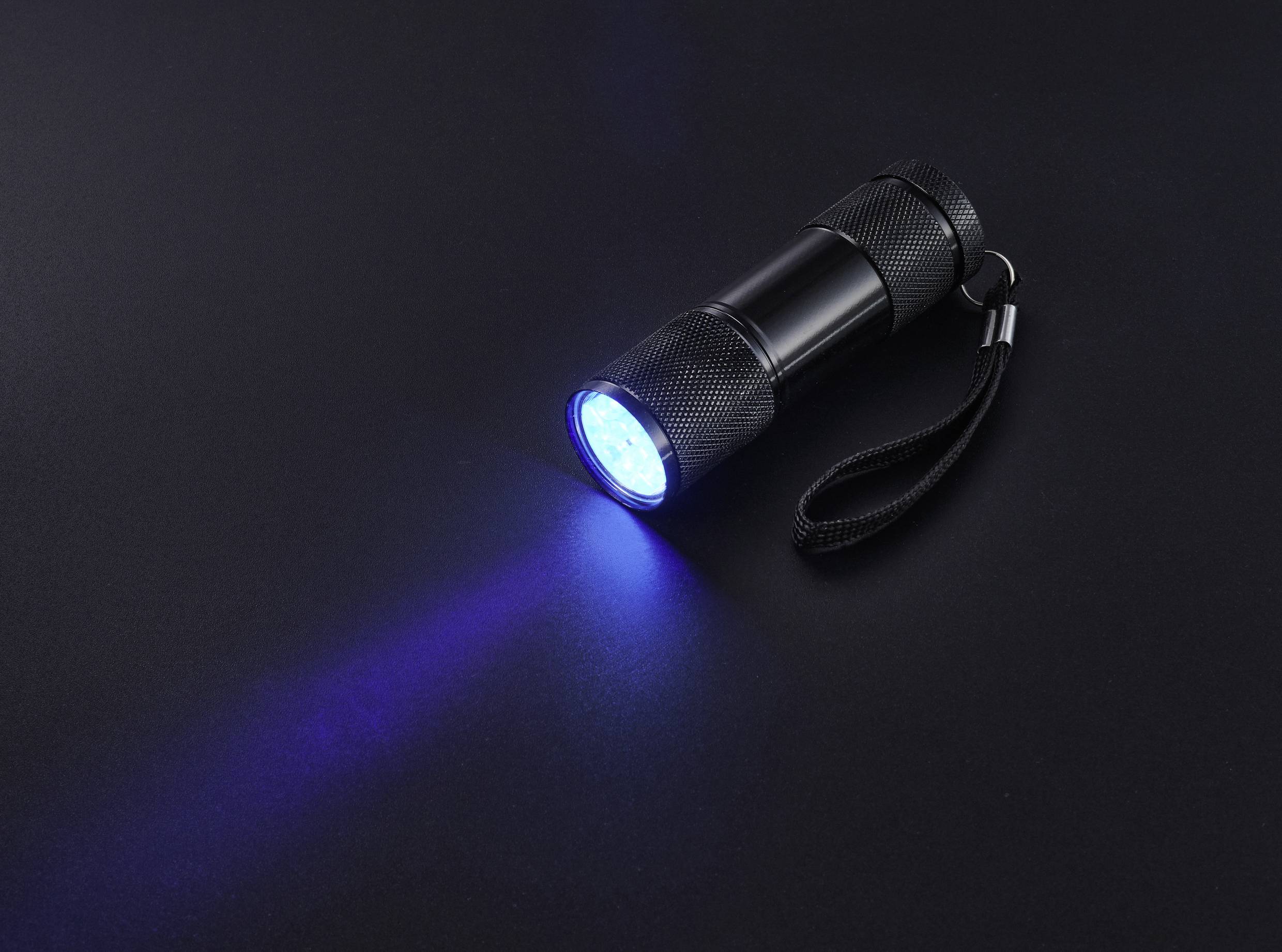 Schwarze Taschenlampe mit blauem Lichtschein auf dunklem Hintergrund, leuchtet nach links.