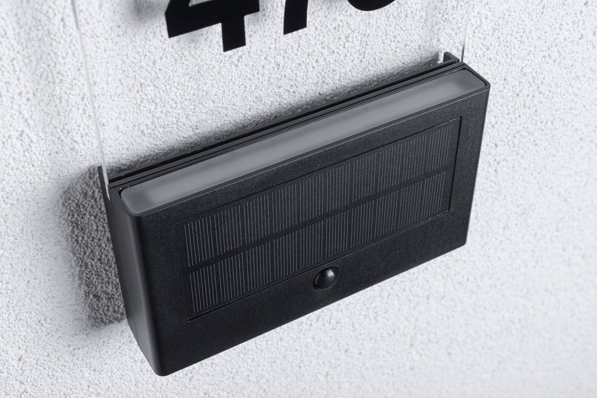 Solarbetriebene Hausnummernleuchte mit schwarzem Solarpanel an einer Wand angebracht.