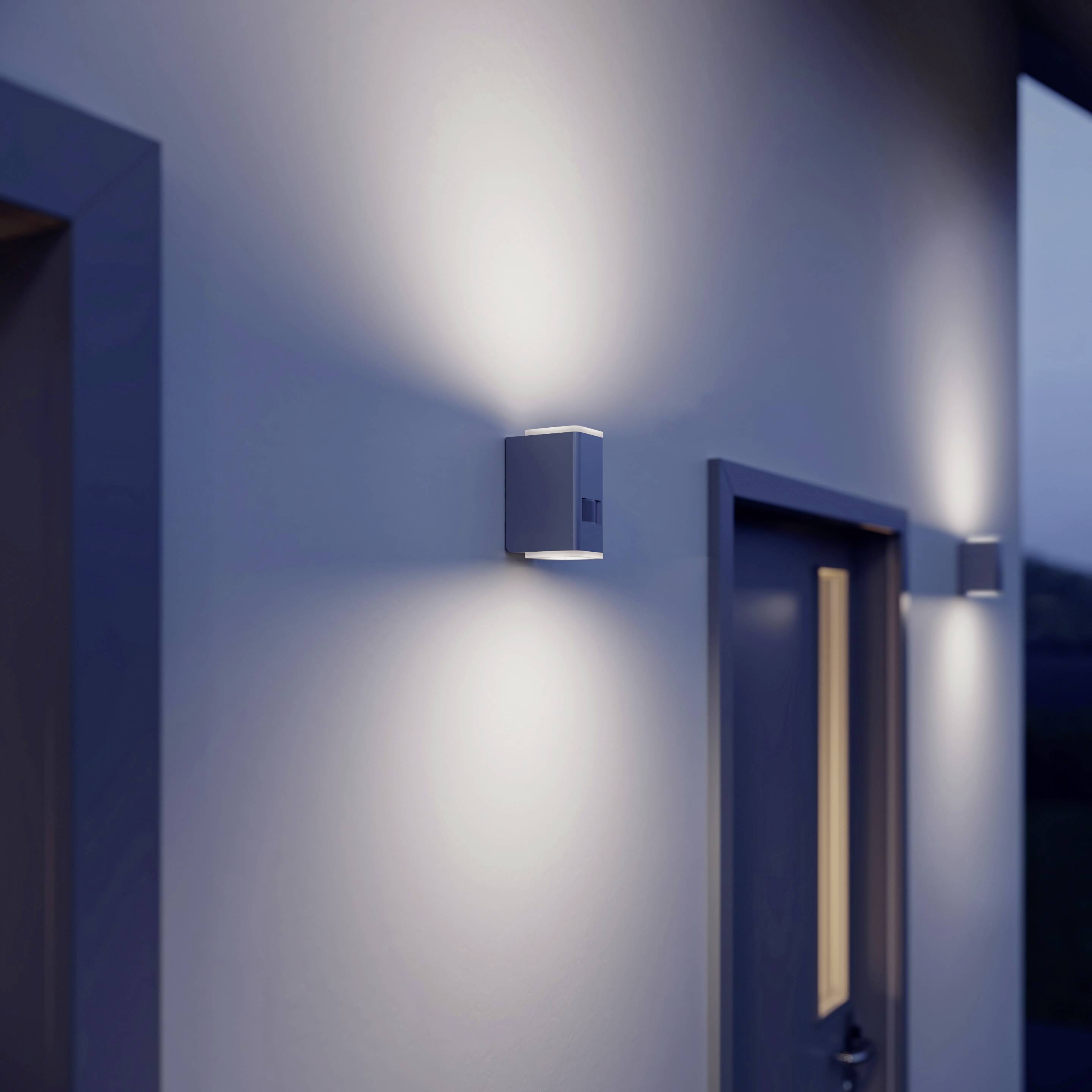 Moderne Außenwand mit quadratischer Lampe, die ein stimmungsvolles, symmetrisches Licht nach oben und unten wirft. Tür daneben.