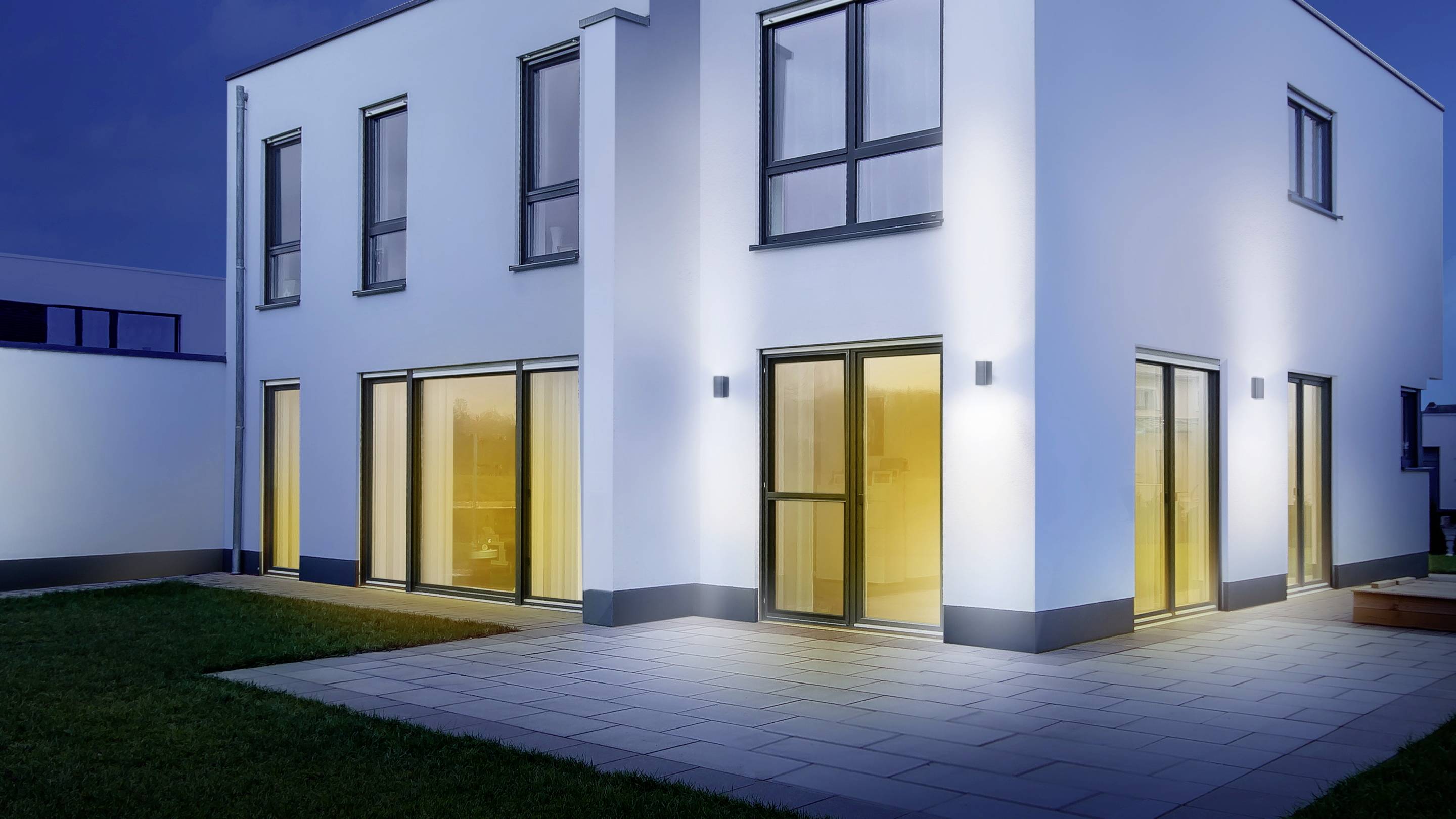 Ein modernes, zweistöckiges Haus bei Nacht mit großen Fenstern und beleuchtetem Innenhof.