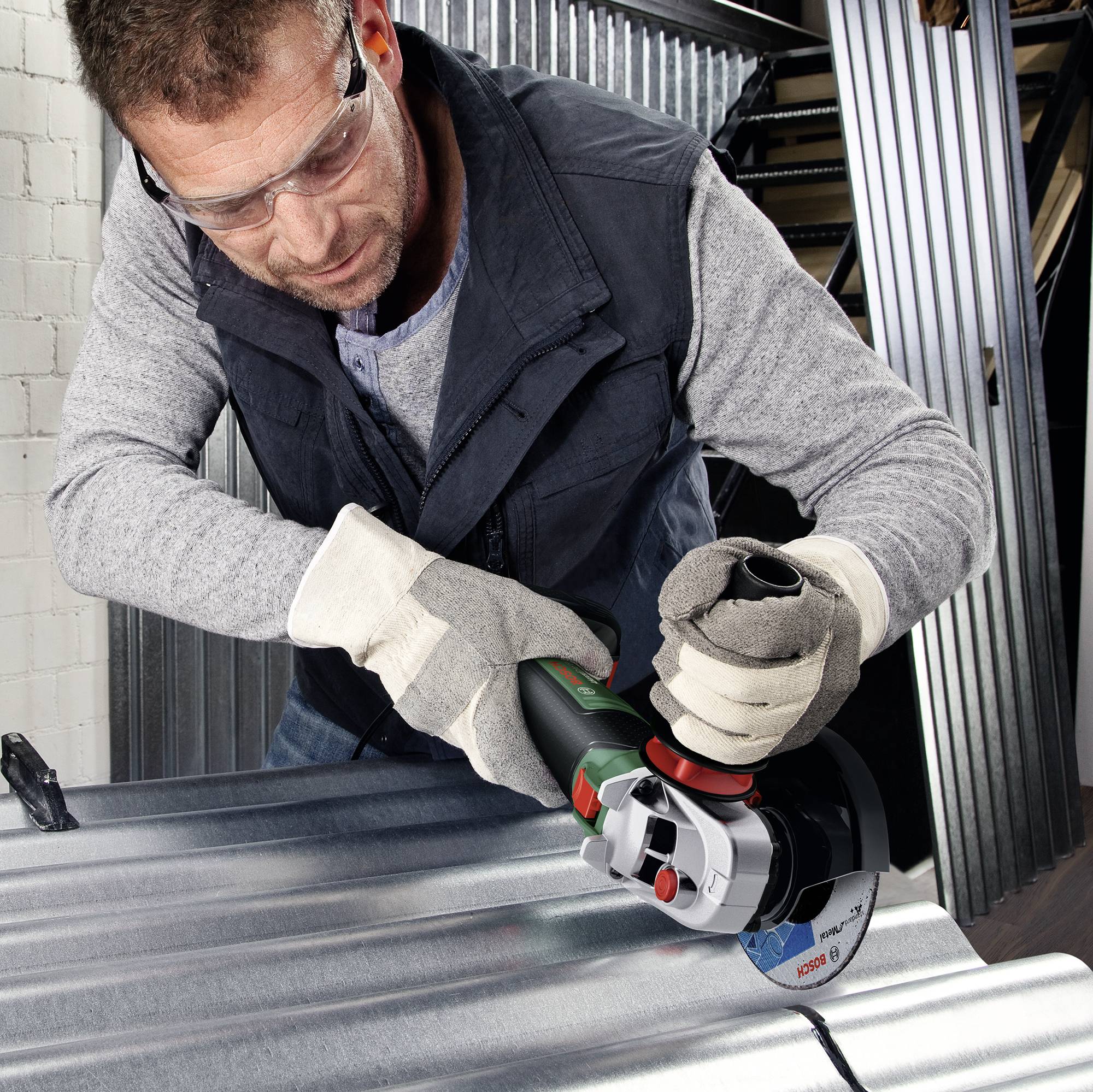 Person mit Schutzbrille schleift Metall mit Winkelschleifer in Werkstatt.