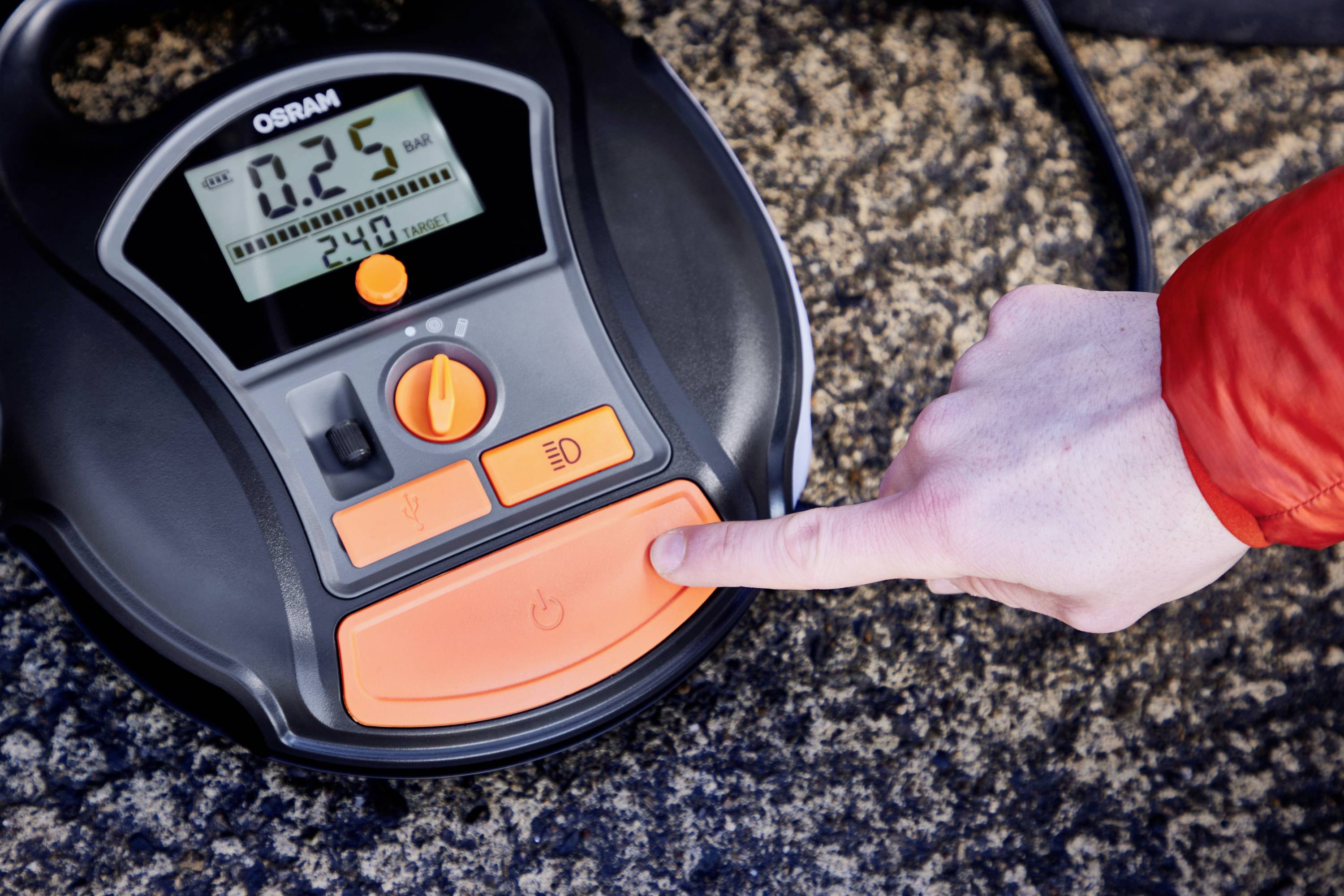 Eine Hand drückt einen Knopf auf einem digitalen Reifendruckmesser von OSRAM. Der Bildschirm zeigt '0.25' bar.