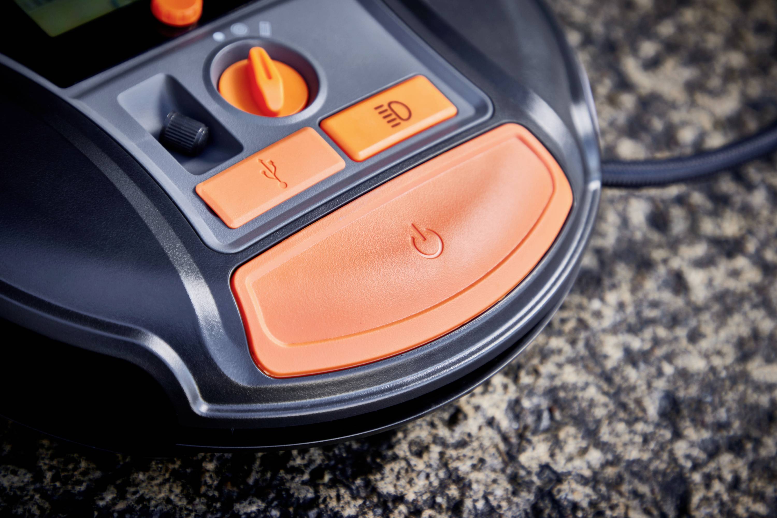 Das Bild zeigt Nahaufnahme eines Automower-Bedienfelds mit orangenen Tasten für verschiedene Funktionen auf einer Steinfläche.