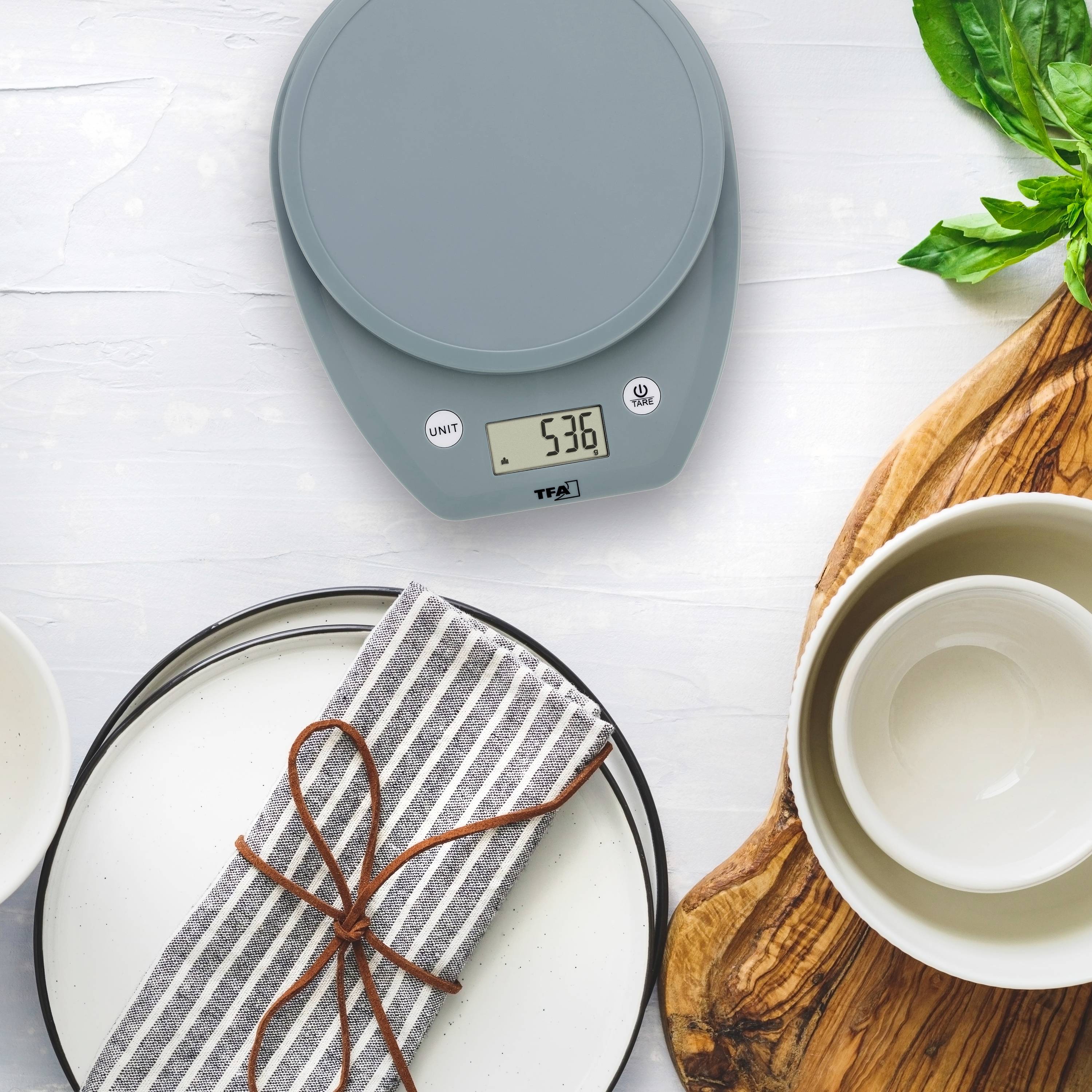 Küchenwaage zeigt '536 g'. Nebenan ein Holzbrett mit einer weißen Schüssel und Teller, dekoriert mit Besteck auf einem gestreiften Tuch.