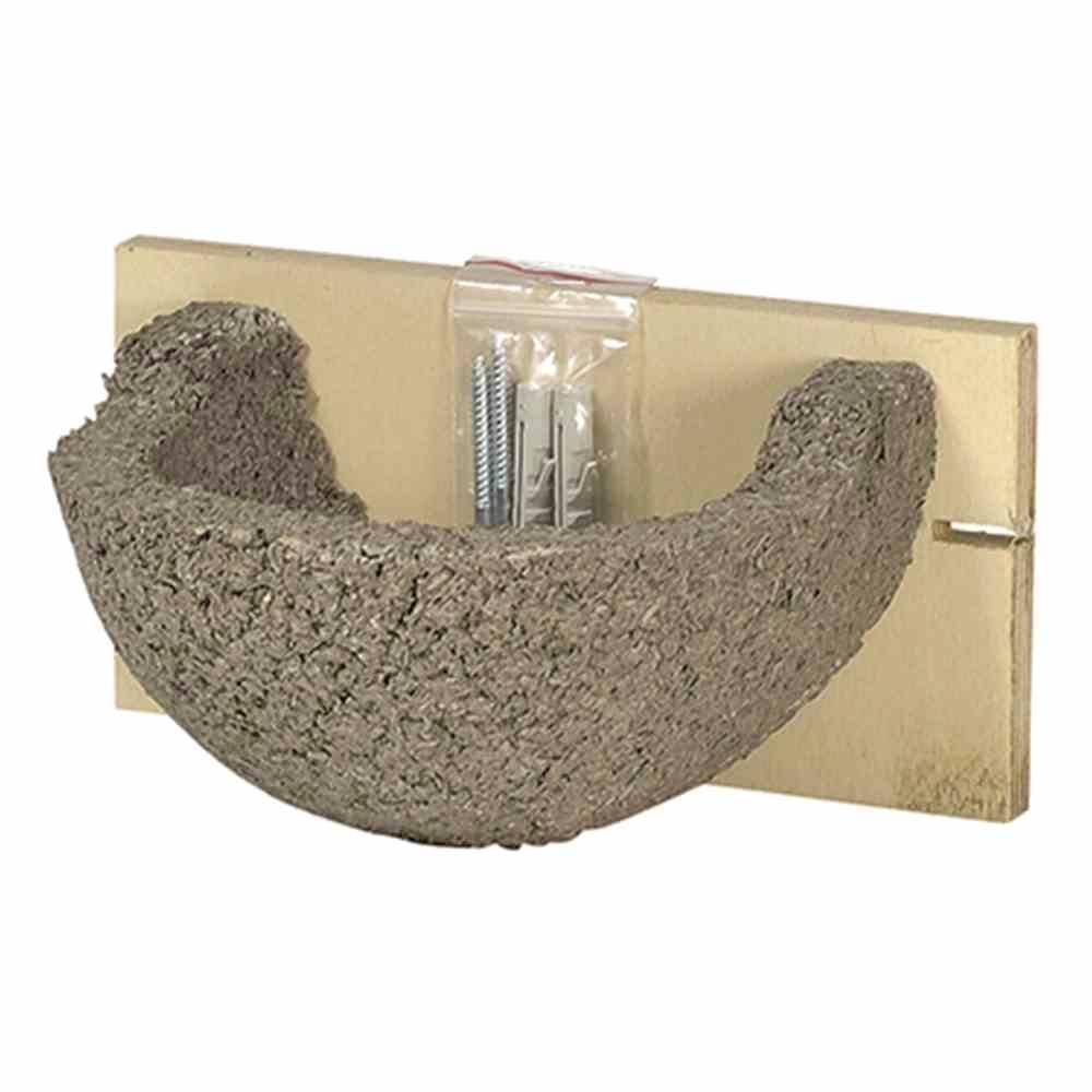 Halbrunder Vogel-Nistkasten aus grauem Material, befestigt auf einer Holzwandplatte. An der Wand oben eine Plastiktüte mit Schrauben.