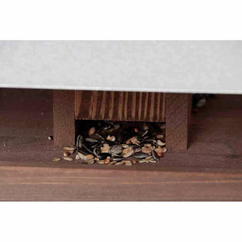 Vogelfutter liegt unter einem Holzdach bereit, mit einer Mischung aus Sonnenblumenkernen und anderen Samen.