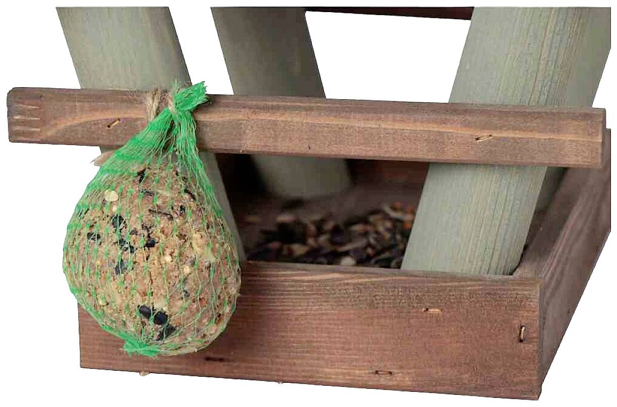 Ein Vogelfutterspender aus Holz mit einem Netz voller Vogelfutter hängt an der Seite. Im Hintergrund sind Holzstreben sichtbar.